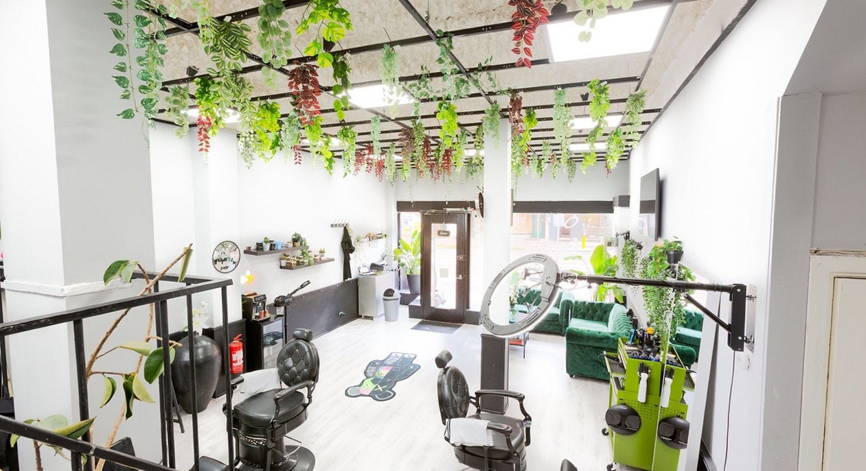 De zaak van achteren gezien: kappersstoelen, ringlamp, hangende planten en de groene bank bij het raam