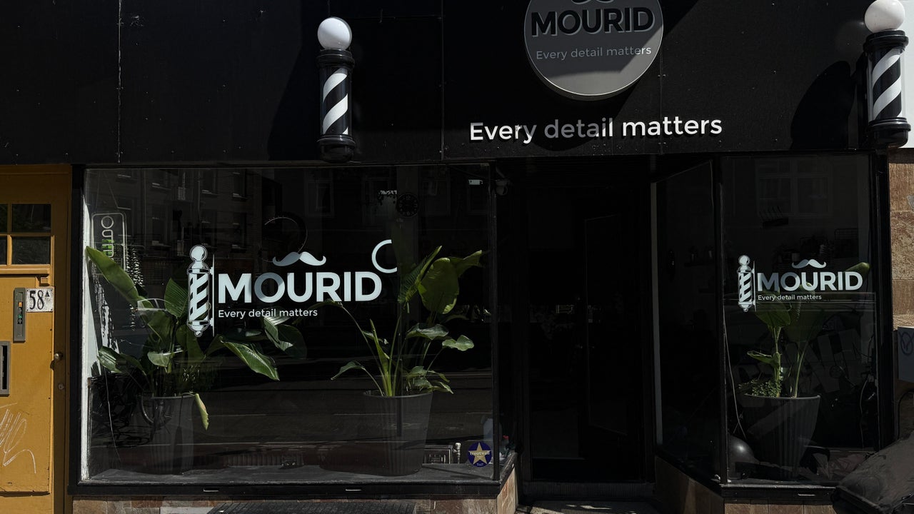 De winkelpui van Mourid in de avond, met het logo op het raam, twee barberpalen en Every detail matters